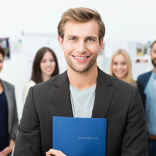 Bild von einem blonden Mann mit einer blauen Bewerbungsmappe im Vordergrund, im Hintergrund sieht man eine Gruppe von Personen.